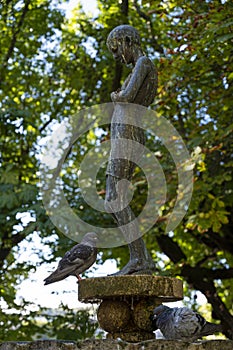 Bronze statue of a girl in the middle of a city garden. Fountain with pigeons taking a bath on a hot day. Alameda gardens