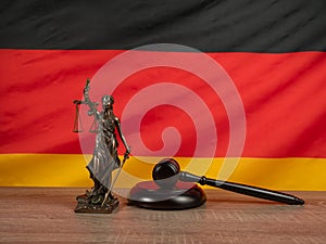 Bronze statue of justice and judges gavel against the background of the German flag.