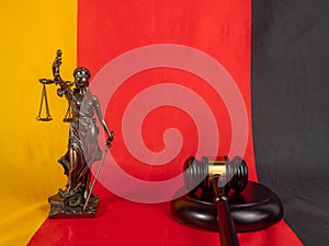 Bronze statue of justice and judges gavel against the background of the German flag.