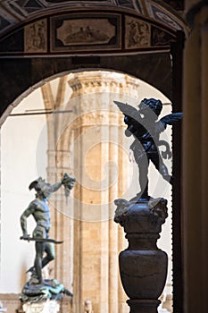 Bronze statue of little angel with background of Perseus with the Head of Medusa in Loggia de` lanzi,  Piazza della Signoria seen