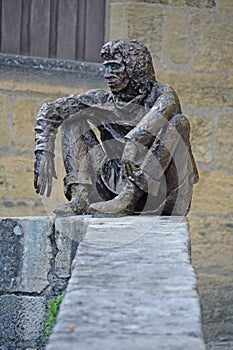 Bronze Statue of man sitting on a wall