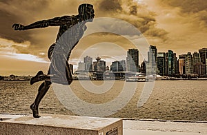 Bronze statue in Stanley Park of running man Harry Jerome in the skyline of Vancouver city in the background