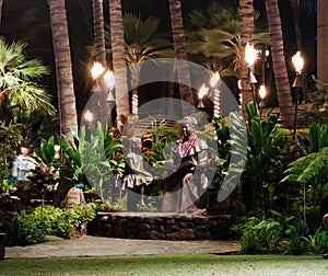 Bronze statue of women with lei and girl, night photo