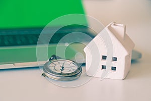 A bronze watch necklace and white ceramic house with laptop background