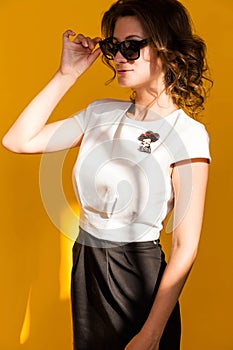 A brooch in the form of a lady in a hat on a white blouse of a brunette girl. Young woman posing on yellow background
