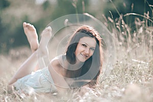 Brooding young woman lying on grass on summer day.