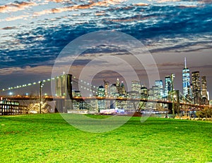 The Brooklyn Bridge at sunset with Manhattan skyline on background and green meadow in foreground, New York City
