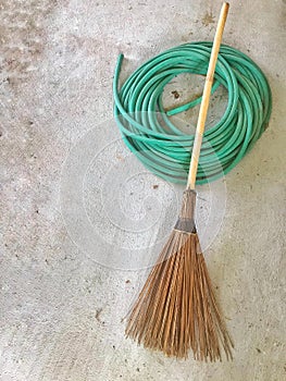 Broom and green hose on cement background