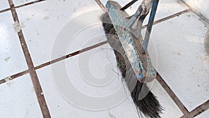 A broom made of wooden handle on the floor leaned against the wall.