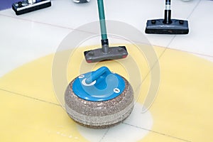 Brooms and stone for curling. view of blue curling stone in outer blue ring of house with broom nearby
