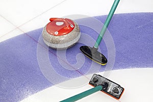 Brooms and stone for curling. view of red curling stone in outer blue ring of house with broom nearby