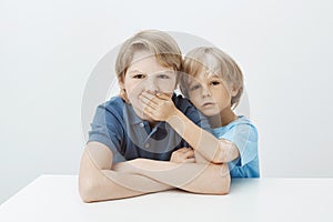 Brother asking to keep secret. Portrait of unhappy annoyed boy sitting at table with hands crossed, frowning while