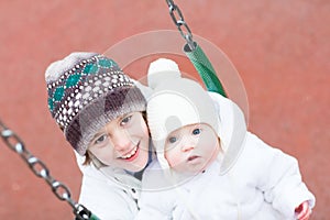 Brother and baby sister swinging in a park