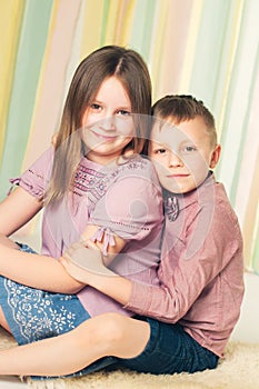 Brother embracing his older sister sitting on a floor