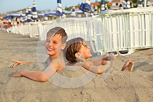 Brother and sister buried in sand on beach