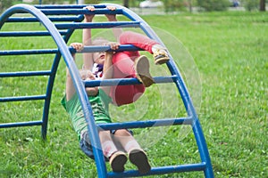 Brother and sister climb and hang on a metal ladde