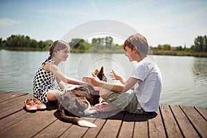 Brother and sister enjoying on the dock of the lake with their dog