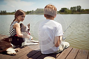 Brother and sister enjoying fishing on the dock with their dog