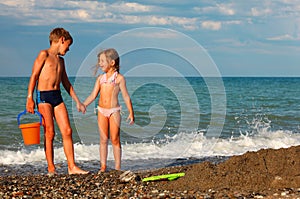 Brother and sister hold hands and stand on beach