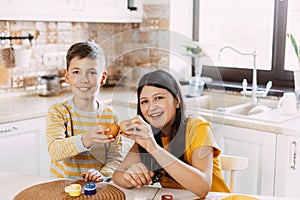 Brother and sister at home in the kitchen paint Easter eggs in different colors for Easter