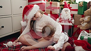 Brother and sister hugging each other sitting on floor by christmas gifts at home