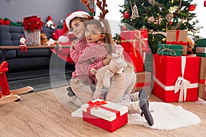 Brother and sister hugging each other sitting on floor by christmas tree at home