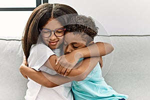 Brother and sister hugging each other sitting on sofa at home