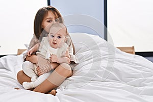 Brother and sister hugging each other sitting together on bed at bedroom