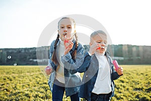 Brother and sister inflate soap bubbles in a green meadow.