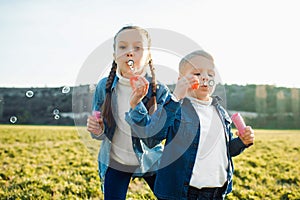 Brother and sister inflate soap bubbles in a green meadow.