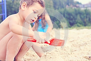 Little cute boy with plastic spatula in hand makes sand castle at the beach.