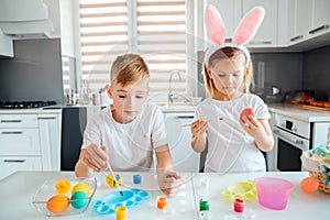 Brother and sister painting Easter eggs. Children make holiday decorations while sitting at the kitchen table.