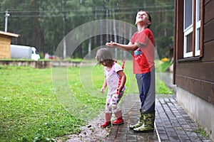 Brother and sister play in rainy weather Children jump in puddle and mud in the rain.