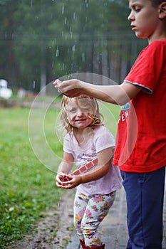 Brother and sister play in rainy weather Children jump in puddle and mud in the rain.