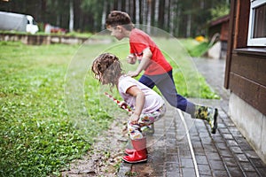 Brother and sister play in rainy weather Children jump in puddle and mud in the rain.