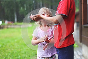 Brother and sister play in rainy weather Children jump in puddle and mud in the rain.