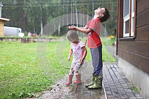 Brother and sister play in rainy weather Children jump in puddle and mud in the rain.