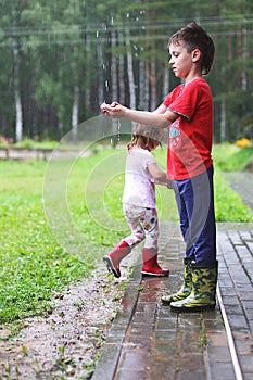 Brother and sister play in rainy weather Children jump in puddle and mud in the rain.