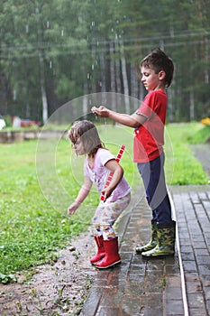 Brother and sister play in rainy weather Children jump in puddle and mud in the rain.