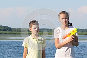 Brother and sister play water pistols on the river