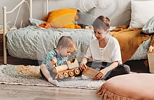 Brother and sister play with wooden toys in children`s room. Children play with a toy designer on the floor