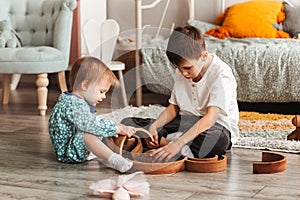 Brother and sister play with wooden toys in children`s room. Children play with a toy designer on the floor