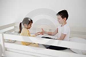 Brother and sister playing a game of rock, scissors, paper on bed at home