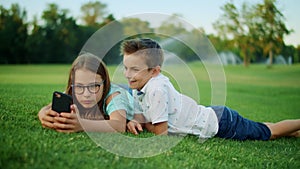 Brother and sister playing games on smartphone in field. Kids using mobile phone