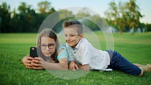 Brother and sister playing games on smartphone in field. Kids using mobile phone