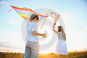 Brother and sister playing with kite and plane at the field on the sunset.