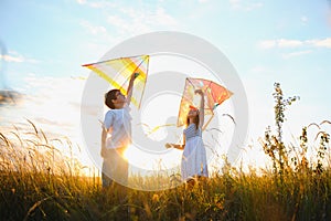 Brother and sister playing with kite and plane at the field on the sunset.