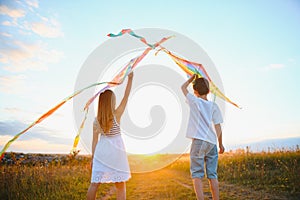 Brother and sister playing with kite and plane at the field on the sunset.