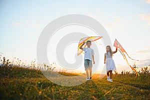 Brother and sister playing with kite and plane at the field on the sunset.