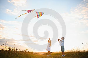 Brother and sister playing with kite and plane at the field on the sunset.